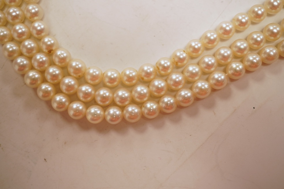 A cultured pearl, ruby and diamond clasp, composed of three rows of cultured pearls measuring approximately 6.9mm diameter, to a white precious metal (tests as 14k) disc-shaped clasp pavé-set with brilliant-cut diamonds